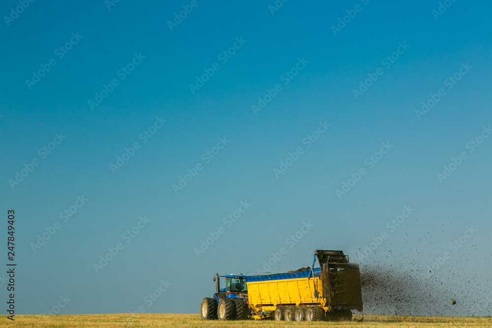 the tractor fertilizes the field with manure. A large trailer. Sowing. Agroindustry.Pole before sowing. Against the sky. yellow tractor. the tractor fertilizes the field with manure. A large trailer. Sowing. Agroindustry.Pole before sowing. Against the sky. yellow tractor.