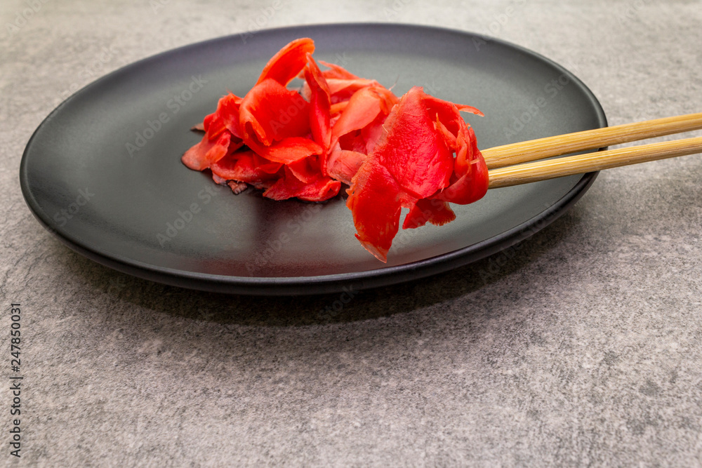 Pickled sushi ginger slices in black plate and chopsticks on stone background, close up Pickled sushi ginger slices in black plate and chopsticks on stone background, close up