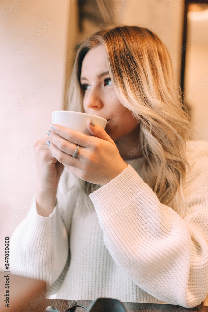 blonde girl in a cozy warm cafe, in a white knitted sweater drinking coffee. blonde girl in a cozy warm cafe, in a white knitted sweater drinking coffee.