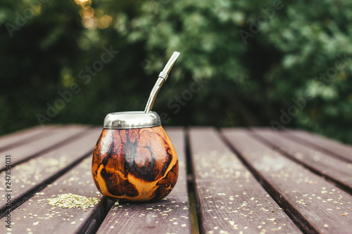 Yerba mate tea in traditional wooden color pumpkin calabash with metal bombilla straw in it, outdoors on garden table. A lot of copy space. photo