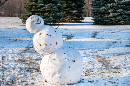 A big lopsided, leaning snowman, evergreens in the blurred soft focused background, copy space. photo