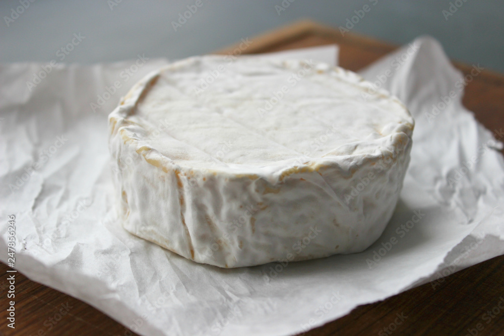 Camembert cheese close-up. Round Camembert cheese on the white paper, the background of the tree. Gourmet cheese, cheese plate, wine food. Camembert cheese. Fresh brie cheese and cut on a wooden Board Camembert cheese close-up. Round Camembert cheese on the white paper, the background of the tree. Gourmet cheese, cheese plate, wine food. Camembert cheese. Fresh brie cheese and cut on a wooden Board