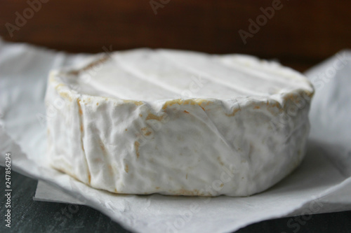 Camembert cheese close-up. Round Camembert cheese on the white paper, the background of the tree. Gourmet cheese, cheese plate, wine food. Camembert cheese. Fresh brie cheese and cut on a wooden Board