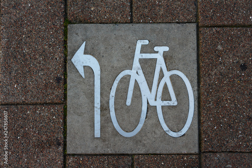 Square metal bicycle path sign, go left arrow, on the cobble stone sidewalk. Top view. Denmark