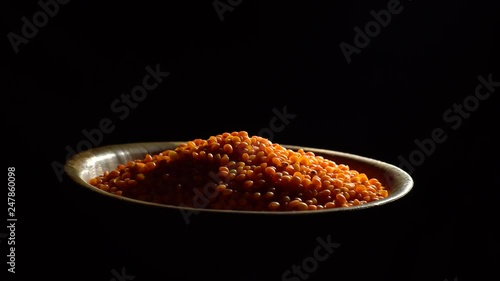 Lentils. Heap of raw uncooked red lentils in bowl in rotation.  Red Chief Lentils, petite crimson lentils - Close up. Food background. black background, studio shot. Healthy organic food diet concept photo