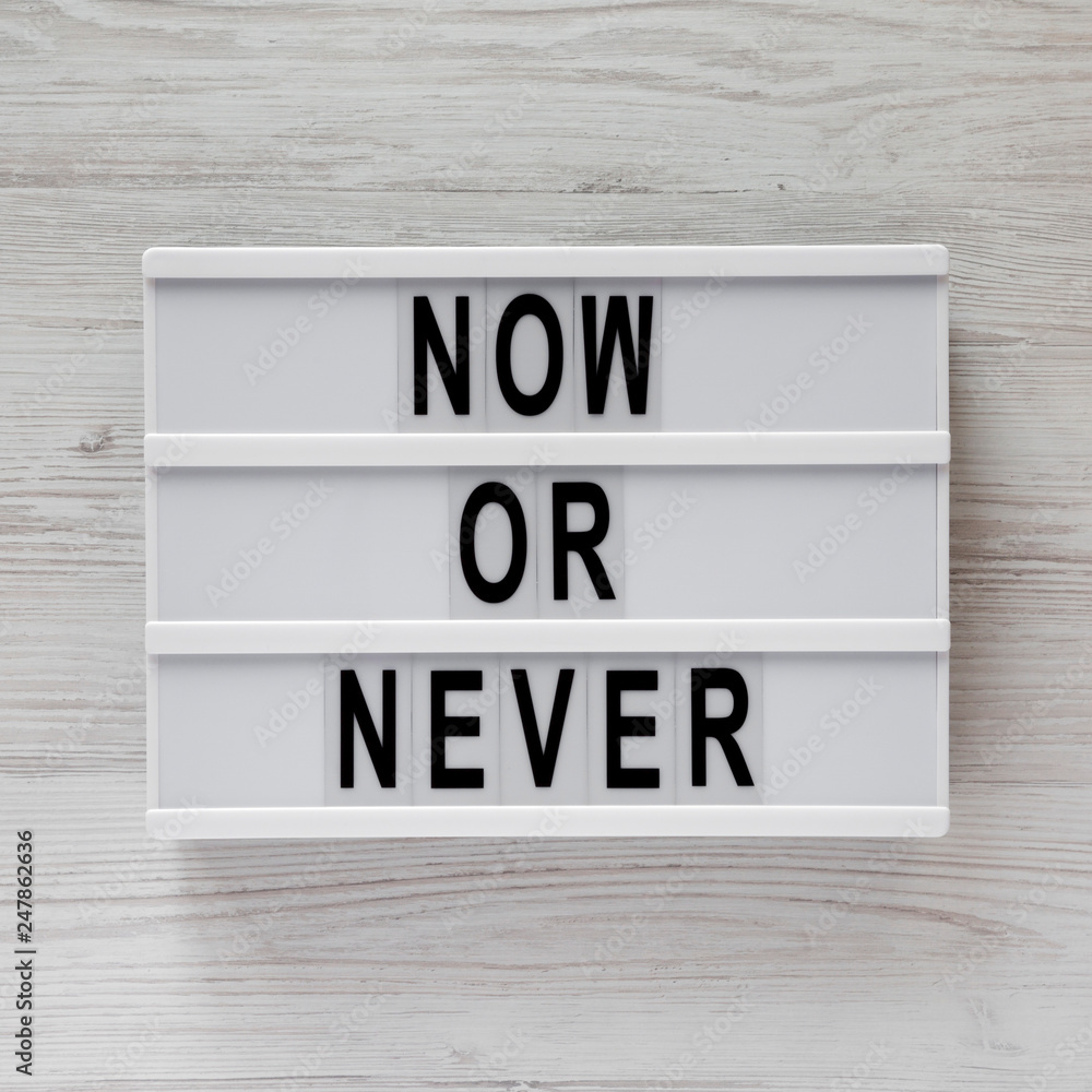 Top view, modern board with text 'Now or never' on a white wooden surface. Flat lay, overhead, from above. Top view, modern board with text 'Now or never' on a white wooden surface. Flat lay, overhead, from above.