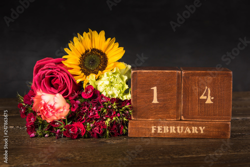 Happy Valentine's Day vintage wooden Perpetual calendar for February 14 on a black background and a bunch of red flowers