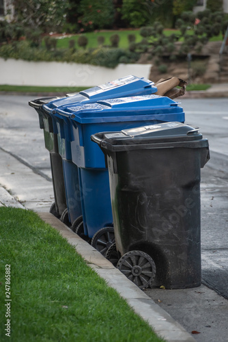 Multi-colored plastic garbage cans full of trash and waiting for pickup on a suburban street