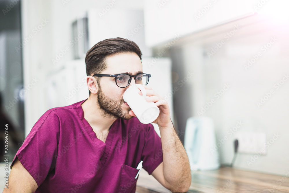 young doctor drinks coffee, tea from a cup after working in a medical office. young doctor drinks coffee, tea from a cup after working in a medical office.