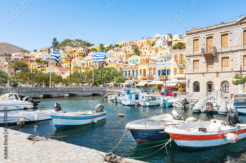 Greek flags, boats and colorful neoclassical houses in harbor town of Symi (Symi Island, Greece)