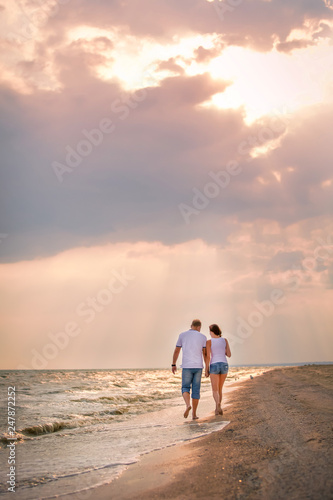 couple in love walks along the sea holding hands surf at sunset, romantic honeymoon, summer