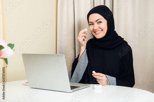 Muslim female talking on the phone while working with laptop computer.