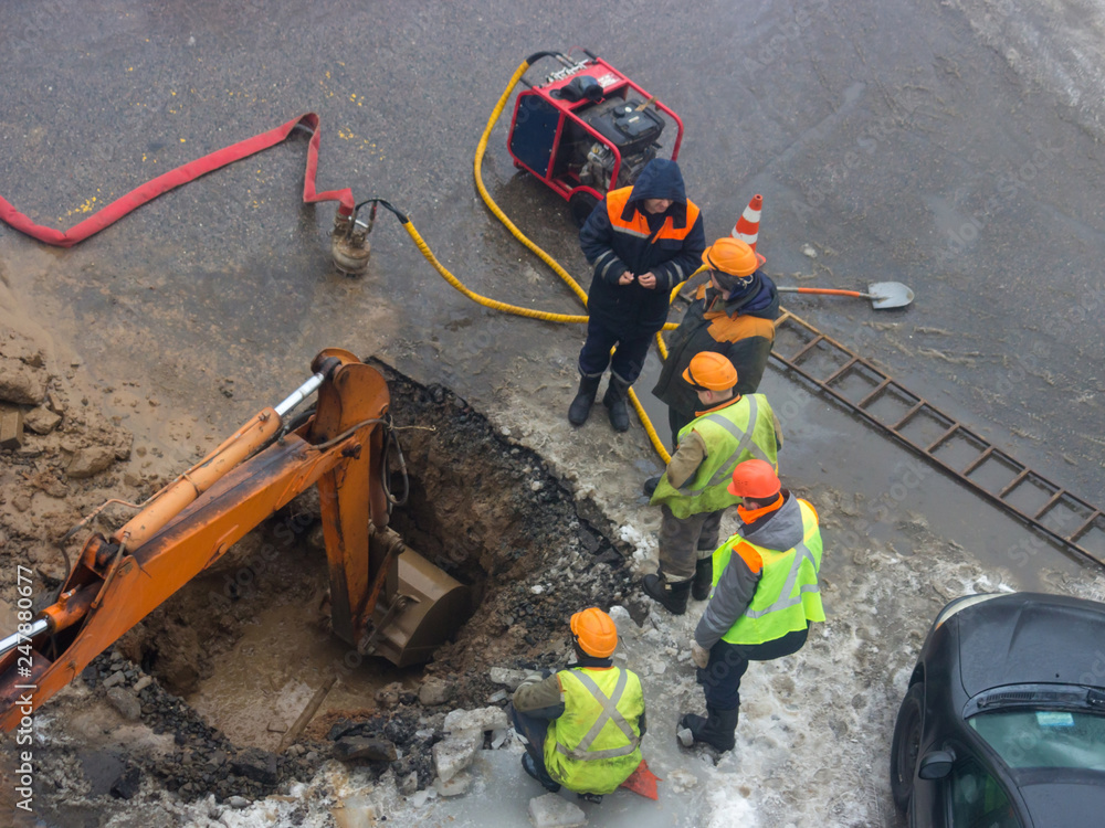 A group of road workers from public utilities in reflective special vests are discussing an emergency when digging a hole to eliminate the leakage of pipes in the middle of winter