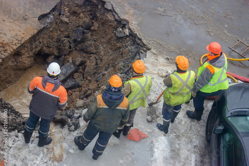 A group of road workers from public utilities in reflective special vests are discussing an emergency when digging a hole to eliminate the leakage of pipes in the middle of winter