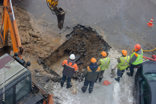 A group of road workers from public utilities in reflective special vests are discussing an emergency when digging a hole to eliminate the leakage of pipes in the middle of winter