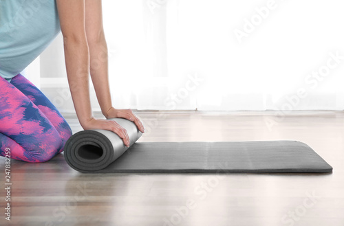 Woman rolling yoga mat on floor indoors, closeup. Space for text