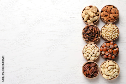 Bowls with different organic nuts and space for text on white wooden background  top view. Snack mix