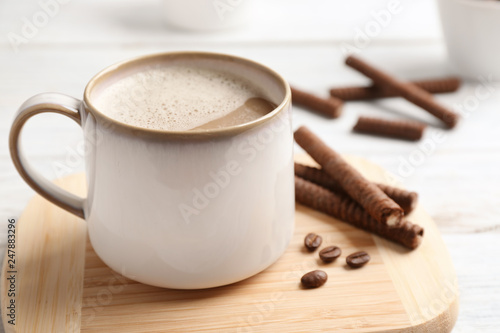 Delicious chocolate wafer rolls and cup of coffee on wooden board, closeup