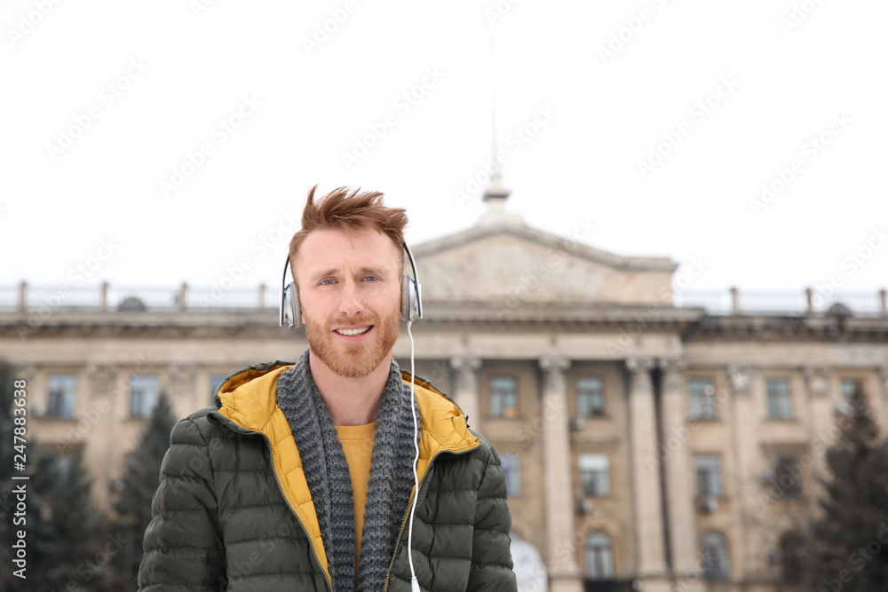 Young man listening to music with headphones outdoors. Space for text