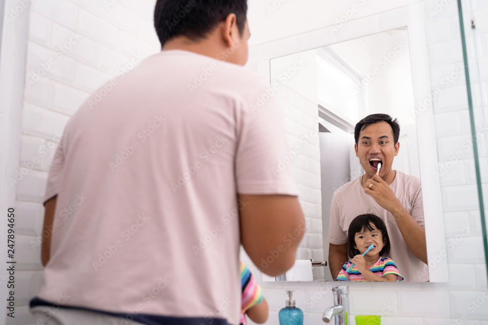 portrait of little girl brushing teeth in bathroom sink with dad portrait of little girl brushing teeth in bathroom sink with dad