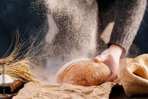 Closeup homemade bread in a man's hand and flour pouring. The concept of healthy food and traditional bakery.