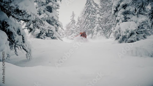 Skier gliding through deep powder snow in the forest during winter. He skies past trees in slow motion with the snow going over his head. photo