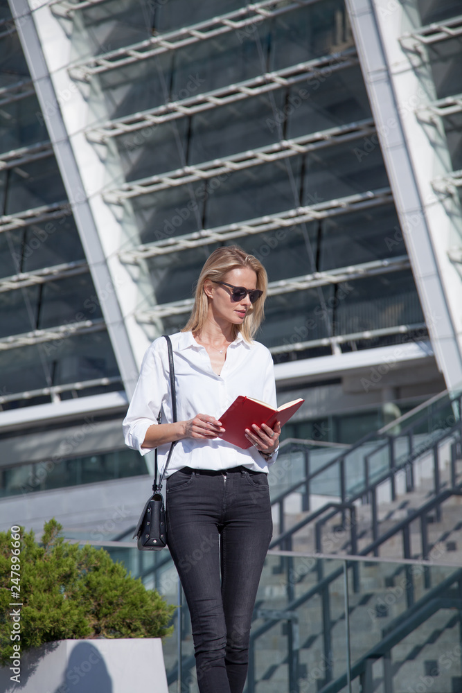 Happy blonde business woman in sunglasses with notebook against of modern building Happy blonde business woman in sunglasses with notebook against of modern building