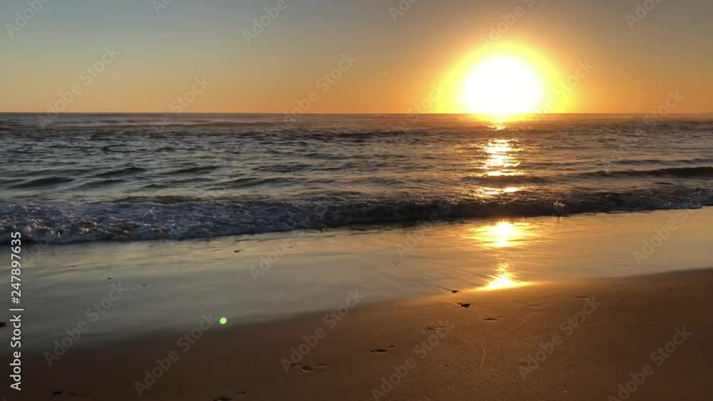 Woman walking along the coastline as sun is setting with waves rolling in Woman walking along the coastline as sun is setting with waves rolling in