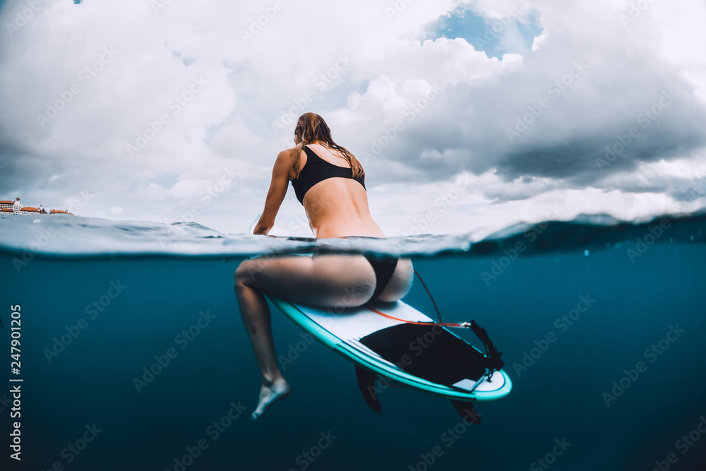 Surfer girl sit at surfboard in blue ocean