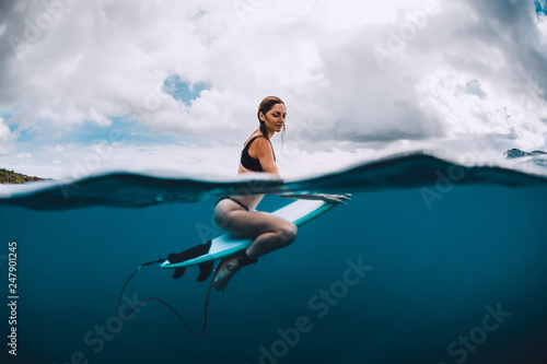 Attractive surf girl sit at surfboard in blue ocean