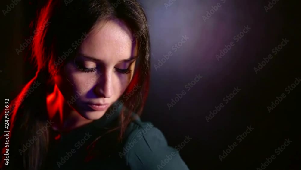 mysterious young pretty woman is looking at camera in dark studio, red soffit is illuminating her mysterious young pretty woman is looking at camera in dark studio, red soffit is illuminating her