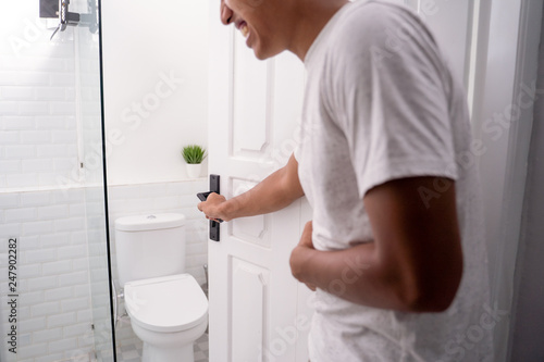 Foto man opening the toilet door and hold his stomach ache
