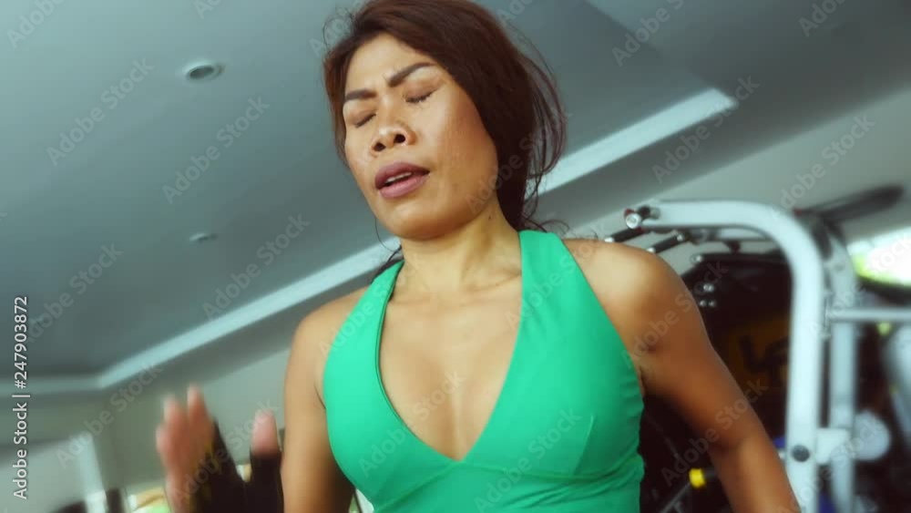 Young fit and athletic Asian Thai woman with fit body running on gym treadmill sweating training hard jogging workout in fitness and healthy lifestyle concept