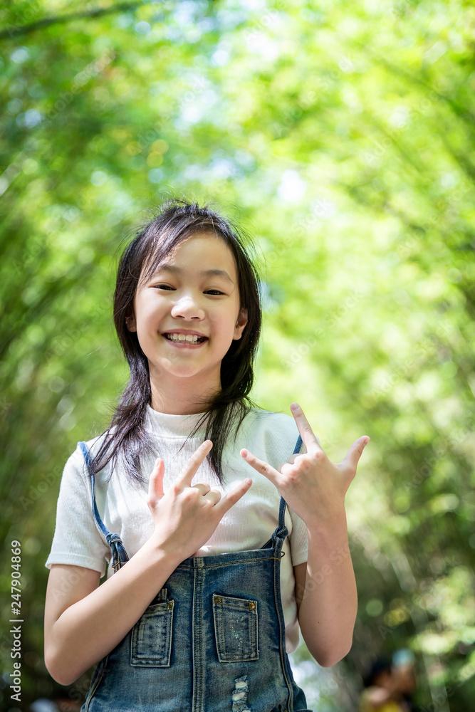 Portrait of smiling little asian girl right sign language meaning I Love You and look at the camera on bamboo forest,green nature background,happy people concept Portrait of smiling little asian girl right sign language meaning I Love You and look at the camera on bamboo forest,green nature background,happy people concept