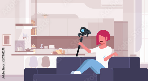 girl blogger recording video on camera woman sitting on couch modern kitchen interior using motorized gimbal stabilizer social media blog concept full length flat horizontal