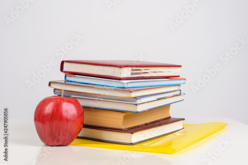 red juicy apple lies on a yellow folder on the table, next to a stack of training books photo