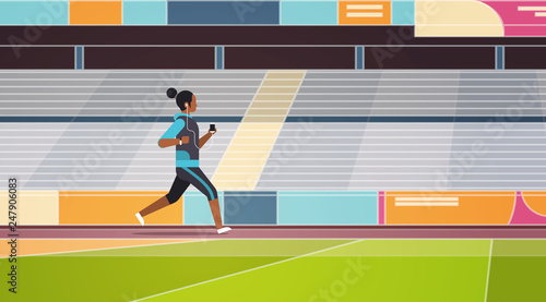 fitness woman running stadium track african american girl listening to music with headphones on smartphone healthy lifestyle concept tribunes background full length flat horizontal
