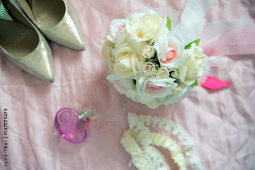 Bridal bouquet of white roses, on a pink bed, short focus, shoes, perfume and lace in the background Bridal bouquet of white roses, on a pink bed, short focus, shoes, perfume and lace in the background