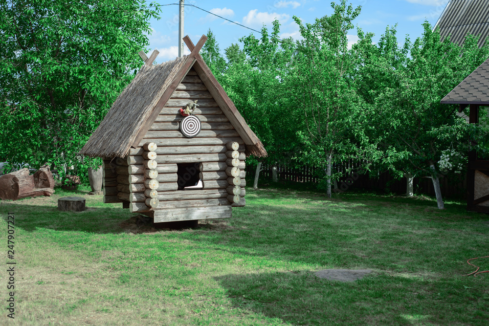 A wooden hut on a green lawn among the trees on the territory of