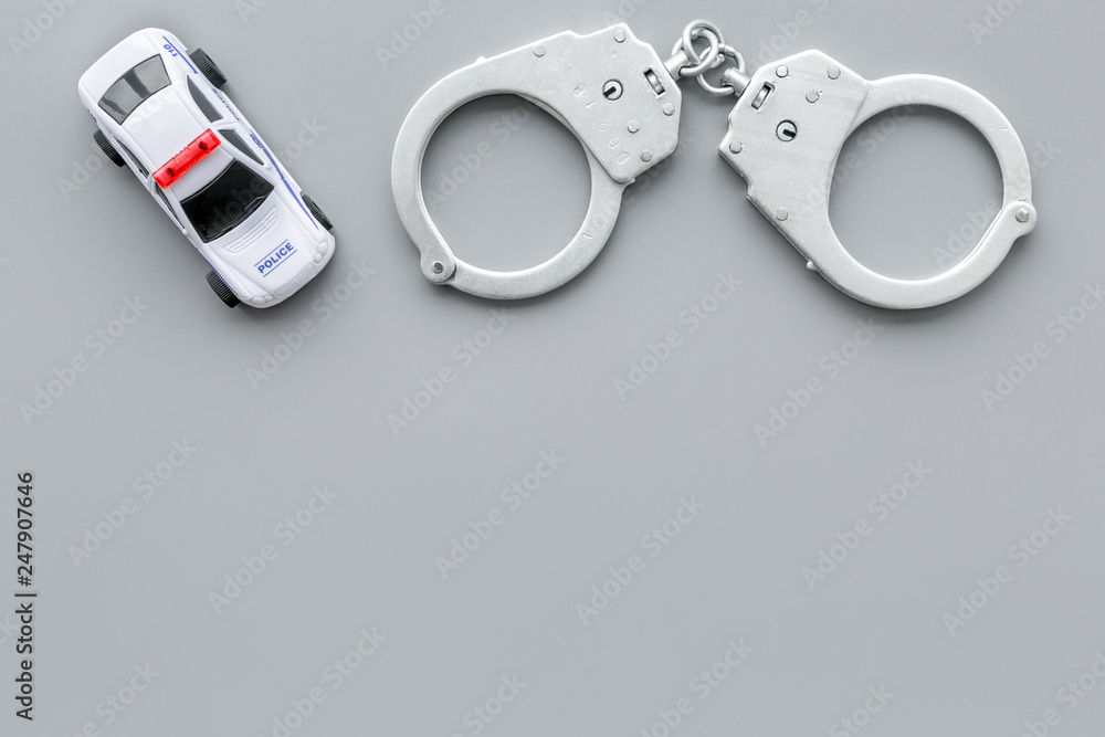 Police concept. Police car toy and handcuff on grey background top view space for text Police concept. Police car toy and handcuff on grey background top view space for text