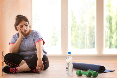 Depressed overweight woman sitting on the floor and doesn't wont to exercise	 photo