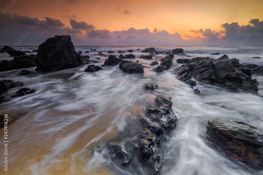 A scenery of sunrise with amazing unique rock formation and beautiful  flow of wave at Kemasik beach, Terangganu Malaysia. Soft focus during long exposure shot.