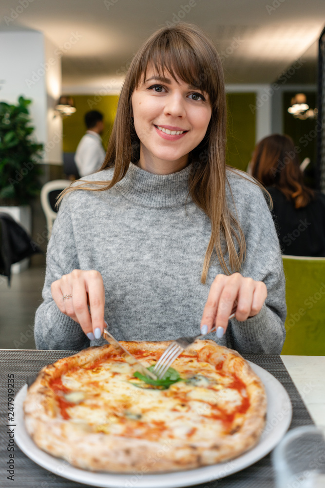Portrait of young woman eating pizza. Neapolitan pizza from wood-burning stove. lunch in an Italian trattoria. Table near to a large window. Margarita and four cheese Portrait of young woman eating pizza. Neapolitan pizza from wood-burning stove. lunch in an Italian trattoria. Table near to a large window. Margarita and four cheese