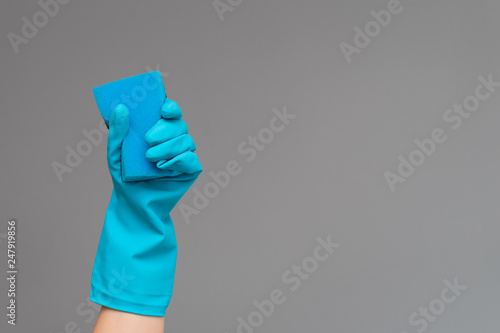 Hand in rubber glove holds color wash sponge on neutral background. The concept of bright spring, spring cleaning.