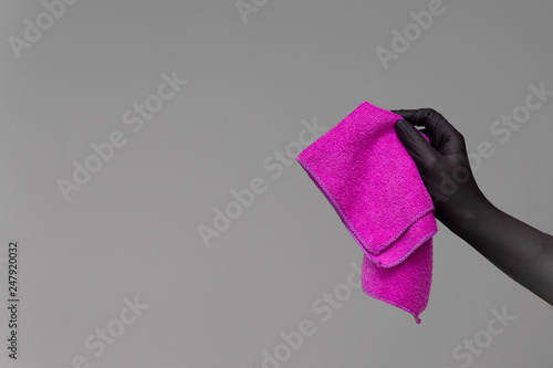 A hand in a rubber glove holds a bright microfiber duster on a neutral background. Сoncept of bright spring, spring cleaning.