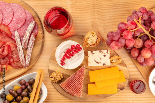 A charcuterie platter and a cheese board, sausages and hams, and a glass of red wine, shot from the top on a wooden background with copy space