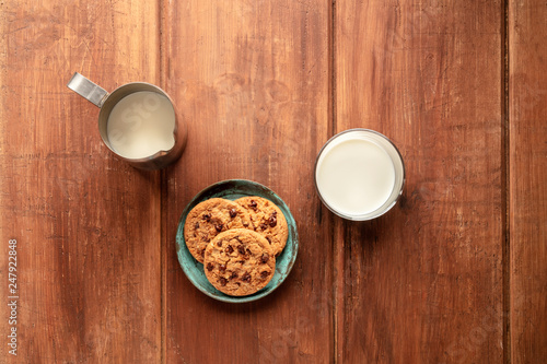 Chocolate chip cookies on a dark rustic wooden background, shot from the top with a milk jug and glass and copy space