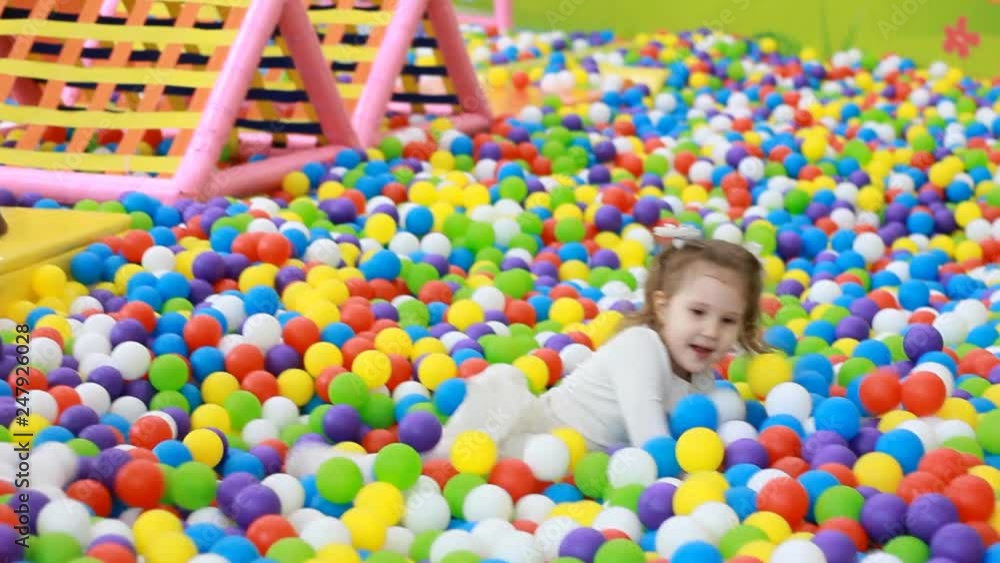 Child jumping in colorful balloons on the playground. Little girl playing games Child jumping in colorful balloons on the playground. Little girl playing games