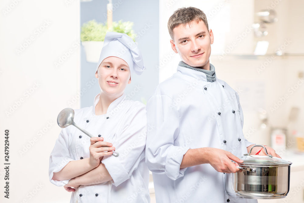 horizontal portrait of a pair of cooks with a pan and a ladle against the background of the kitchen