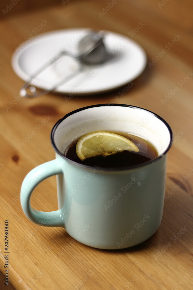 Hot warming tea with lemon in a light blue mug with a brewed tea strainer on a table with a wooden texture Hot warming tea with lemon in a light blue mug with a brewed tea strainer on a table with a wooden texture